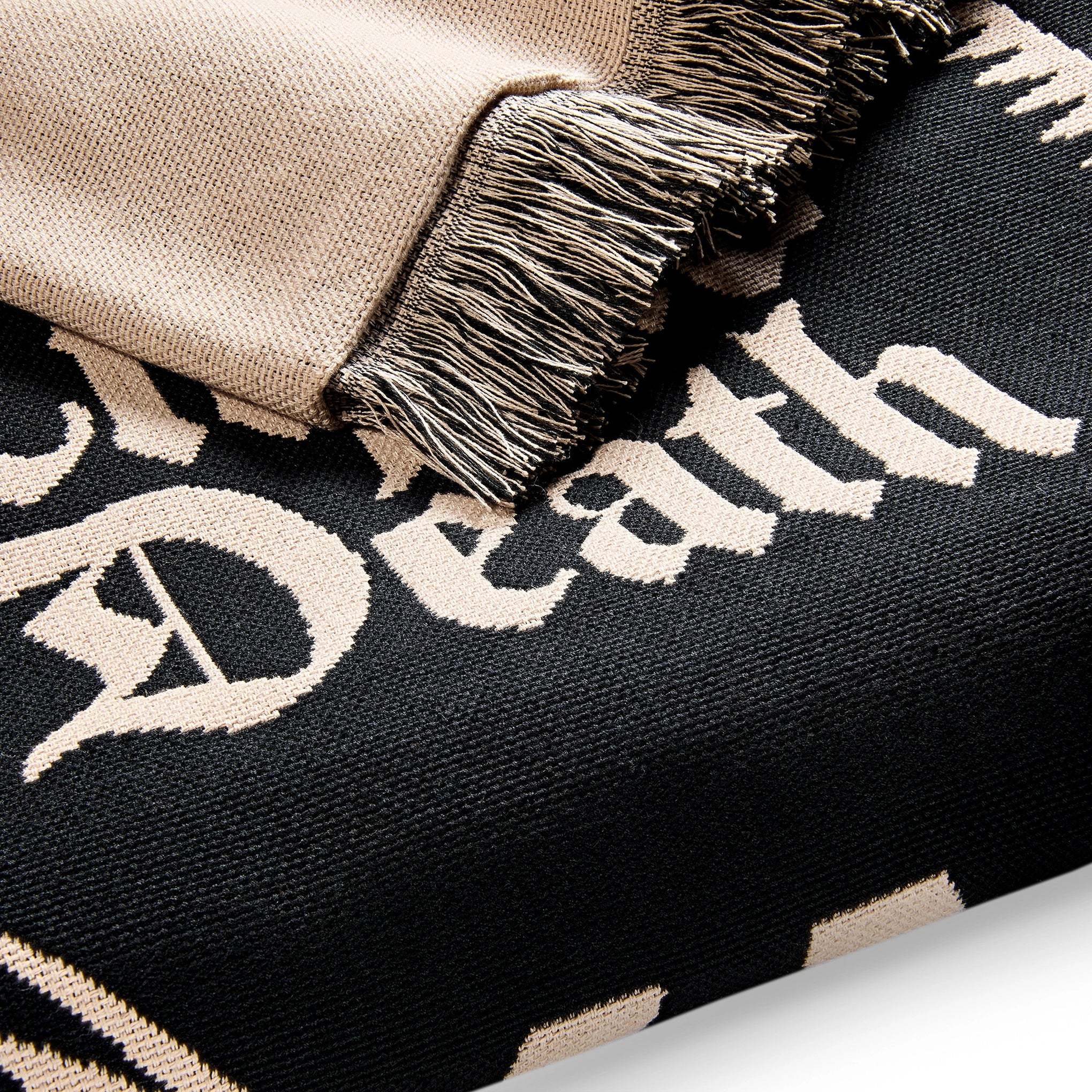 Close-up of a black and beige blanket with 'Death' text and fringed edge.