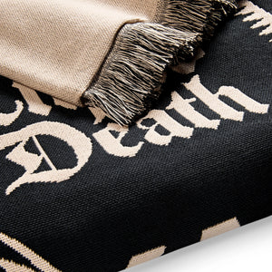 Close-up of a black and beige blanket with 'Death' text and fringed edge.