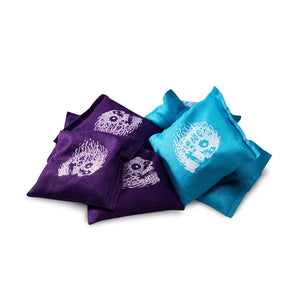 Purple and blue cornhole bags with white designs on a white background